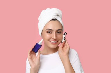 Pembe arka planda tekrar kullanılabilir pamuk pedi ve damlatıcı şişesi olan genç bir kadın.