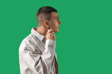 İşitme sorunu olan genç bir adam ve yeşil arka planı büyütüyor.