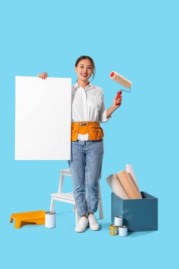 Boya silindirli ve mavi arka planda boş posteri olan Asyalı bir kadın dekoratör.