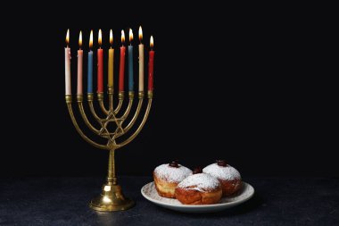 Siyah arka planda Hanuka için şamdanlı ve lezzetli çörekler.