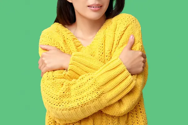 Young Asian woman hugging herself on green background, closeup