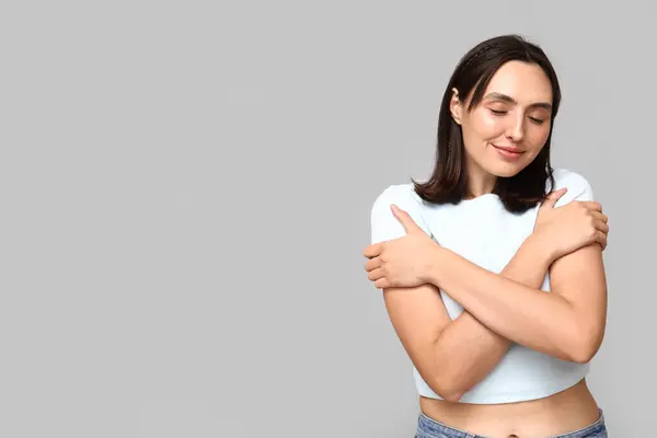 Young woman hugging herself on light background