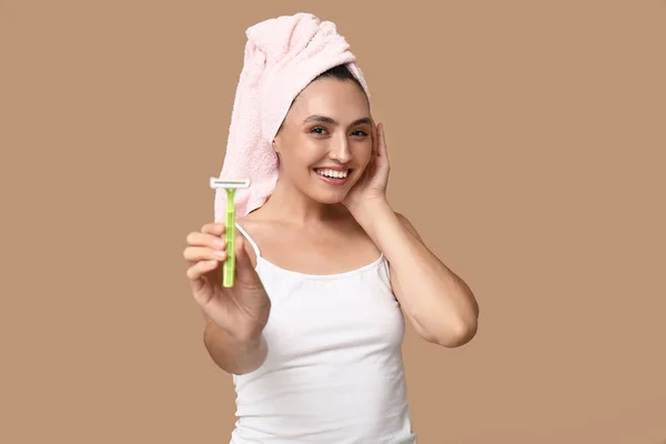 Young woman with razor on brown background