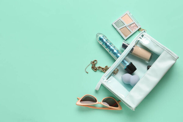 Cosmetic bag with different makeup products, stylish sunglasses and vibrator from sex shop on turquoise background