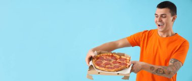 Açık mavi arka planda leziz pizzası olan mutlu genç bir adam.