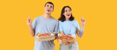Lezzetli pizzaları olan mutlu genç çift sarı arka plandaki bir şeyi işaret ediyor.