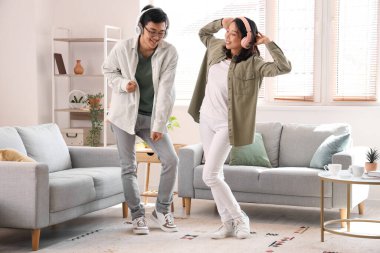 Kulaklıklı genç Asyalı arkadaşlar evde dans ediyor.