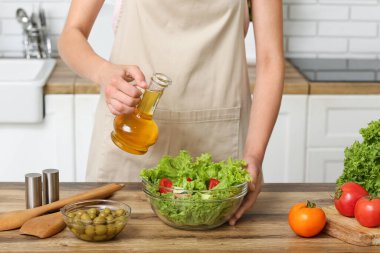 Mutfaktaki masada lezzetli salata ile zeytinyağı ekleyen bir kadın.