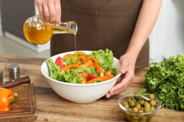 Mutfaktaki masada lezzetli salata ile zeytinyağı ekleyen bir kadın.