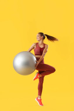 Sarı arka planda fitball antrenmanı yapan genç bir bayan.
