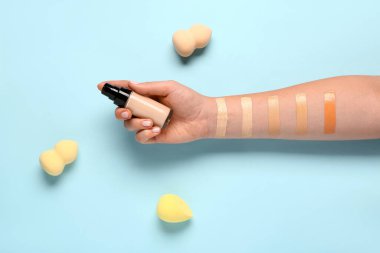 Makyaj malzemesi şişesi, süngerler ve mavi arka planda örnekler olan bir kadın eli.