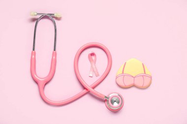 Kalp şeklinde kurabiye, sütyen, pembe kurdele ve leylak arkaplanda steteskop. Göğüs kanseri farkındalığı konsepti