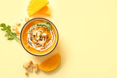 Bir kase lezzetli balkabağı kremalı çorba, kızarmış ekmek ve sarı arka planda roka.