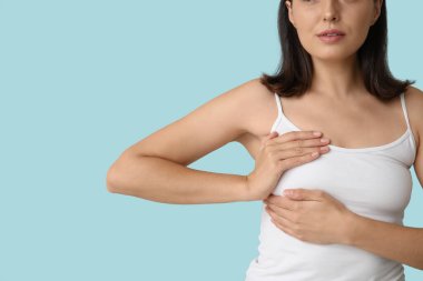 Mavi arka planda göğüslerini kontrol eden genç bir kadın, yakın plan. Kanser farkındalığı kavramı