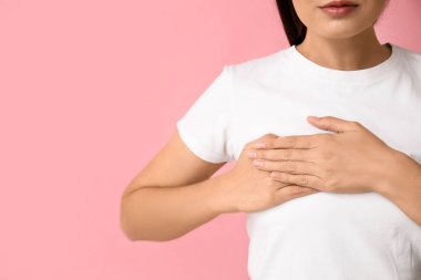 Pembe arka planda göğüslerini kontrol eden genç bir kadın, yakın plan. Kanser farkındalığı kavramı
