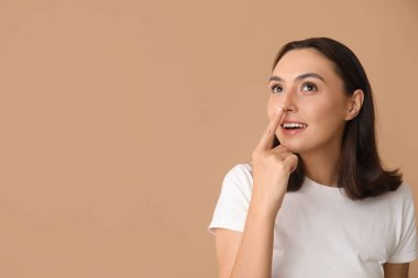 Bej arka planda burnuna dokunan genç kadın, yakın plan.