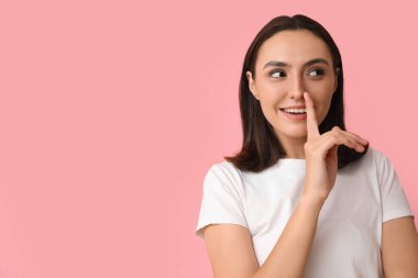 Genç bir kadın pembe arka planda burnuna dokunuyor.