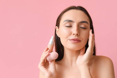 Makyaj temeli ve pembe arka planda süngeri olan genç kadın, yakın plan.