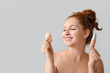 Makyaj temeli ve arka planda süngeri olan genç kızıl saçlı kadın, yakın plan.