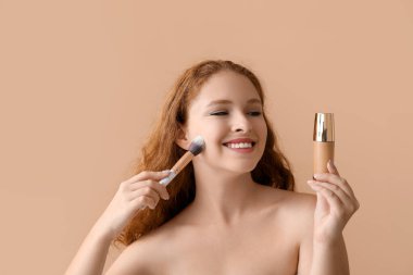 Makyaj temeli olan genç kızıl saçlı kadın ve bej arka planda fırça, yakın plan.