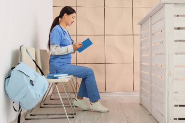 Klinikte kitap okuyan Asyalı kadın stajyer.