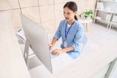 Kadın Asyalı stajyer klinikteki resepsiyonda bilgisayarla çalışıyor.