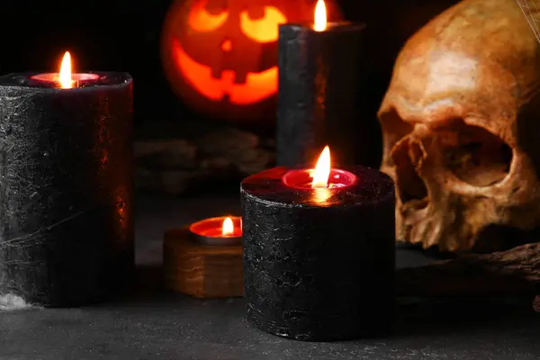 Composition with burning candles and skull for Halloween celebration on black background, closeup