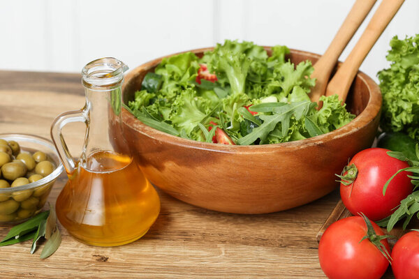 Кувшин с оливковым маслом, овощи и свежий салат на столе на кухне
