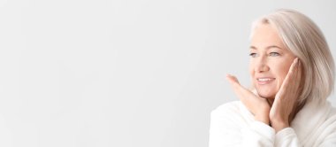 Olgun bir kadın hafif arka planda yüz masajı yapıyor ve mesaj için kendine yer açıyor.