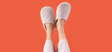 Turuncu arka planda yumuşak terlikler giyen kadın bacakları.