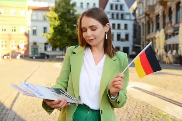 Young woman with flag of Germany and magazines on city street