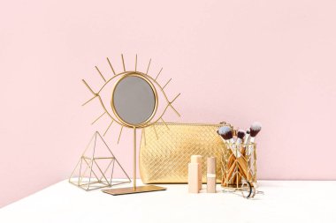 Kozmetik çanta, makyaj malzemeleri ve aynalar odada pembe duvarın yanında.