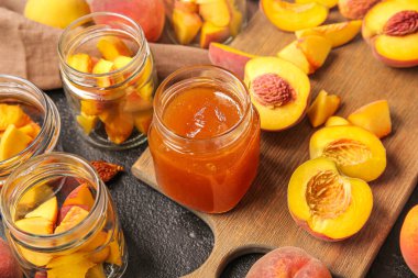 Tatlı şeftali reçelli kavanozlar ve siyah arka planda taze meyveler.