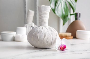 Bitkisel masaj çantası ve orkide çiçeği ışık masasında.