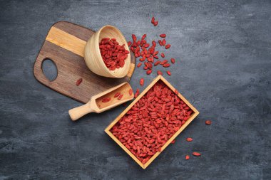 Ahşap kutu ve siyah arka planda kırmızı kurutulmuş goji üzümlü kase.