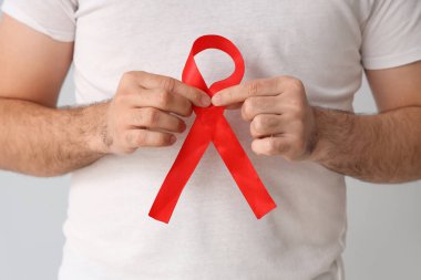 Gri arka planda kırmızı kurdeleli genç adam, yakın plan. Dünya AIDS Günü konsepti