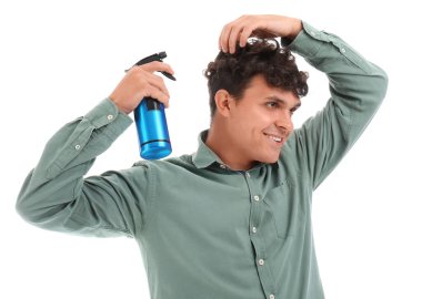 Kıvırcık saçlarına beyaz arka plana saç spreyi sıkan yakışıklı bir genç.