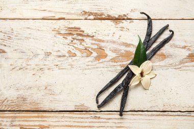 Beyaz ahşap zemin üzerinde Aromatik vanilya çubukları ve çiçek