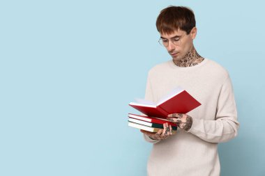 Mavi arka planda kitap okuyan dövmeli genç bir adam.