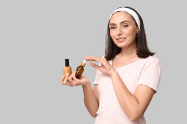 Hafif arka planda kozmetik ürünleri şişeleri olan genç bir kadın.