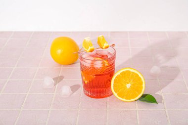 Lezzetli bir bardak Negroni kokteyli, buz küpleri ve portakallar renkli fayans masasında.