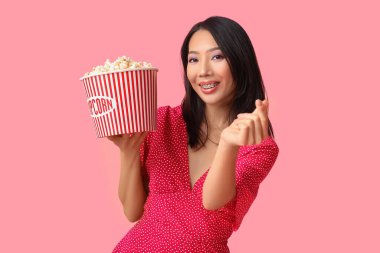 Pembe arka planda patlamış mısır kovası olan genç Asyalı kadın.