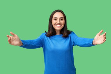 Genç bir kadın yeşil arka planda kucaklanmak için kollarını açıyor