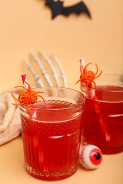 Cadılar Bayramı 'nda bej arka planda örümcekler ve şekerler olan lezzetli kırmızı kokteyller. Yakın plan.