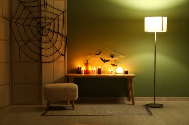 Yanan mumlar, bank, lamba, katlanan ekran ve karanlık odada yeşil duvarın yanındaki Cadılar Bayramı dekorlu masa.