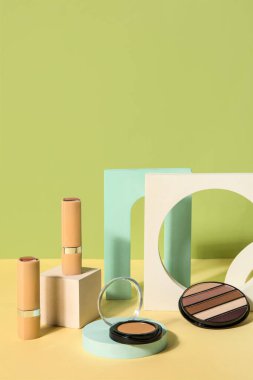 Yeşil duvarın yanındaki masada podyumlarla dekoratif kozmetik ürünler.