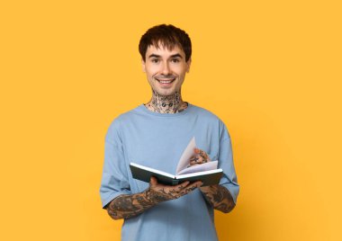 Sarı arka planda kitabı olan dövmeli genç bir adam.