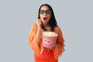 Beyaz arka planda patlamış mısır kovası olan 3 boyutlu gözlüklü genç Asyalı kadın.