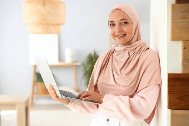 Evde dizüstü bilgisayar kullanan olgun Müslüman kadın.