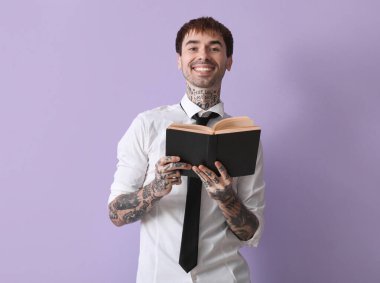 Gömlekli genç adam leylak arkaplan kitabı okuyor.